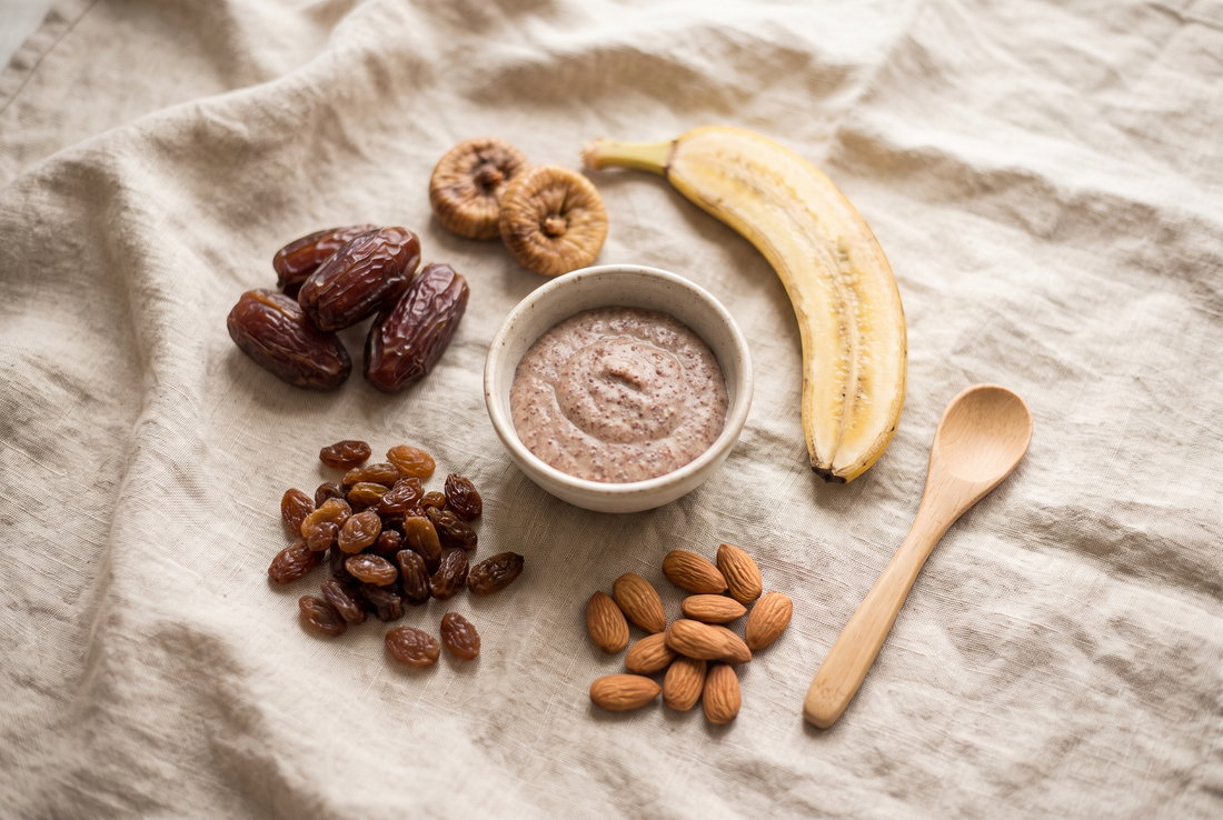 Overhead flat lay of dates, dried figs, raisins, ragi porridge and soaked almonds on a natural linen cloth